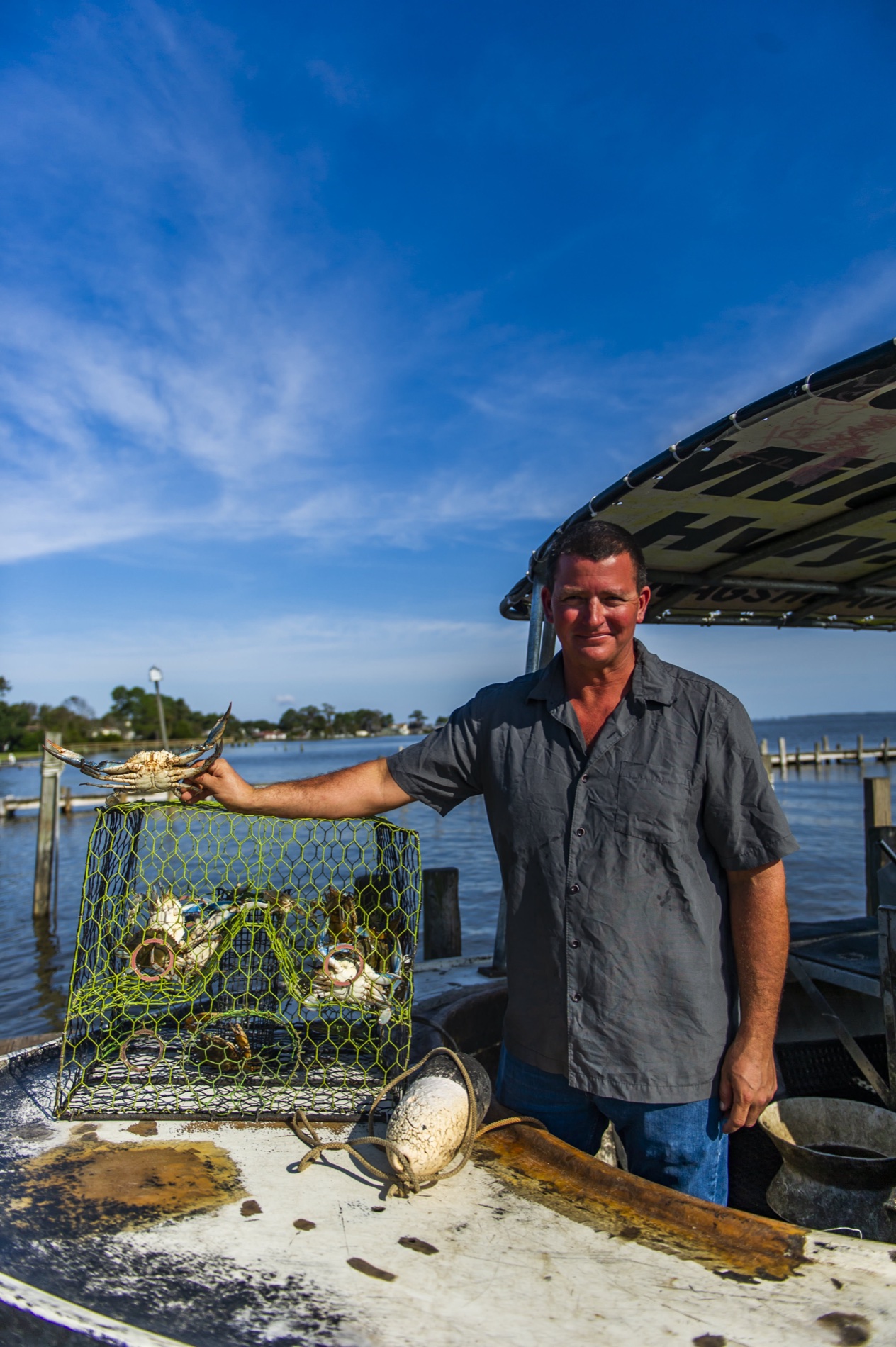 Hunter holding a blue crab beside a full crab pot on his boat